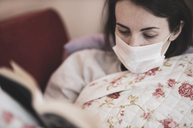 A woman reads a book while wearing a face mask