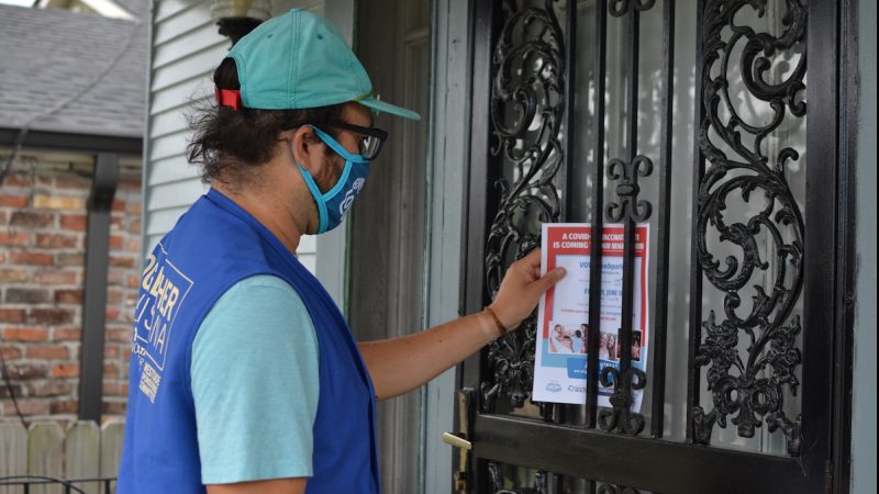 Together Louisiana volunteer Hugo Martinez leaves an informational flyer on a door about a COVID-19 vaccination event in New Orleans.