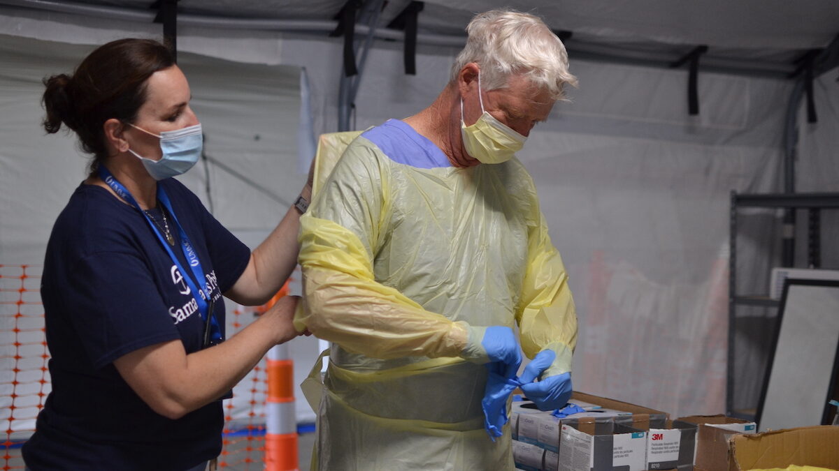 Nurse Kelly Sites helps Nurse John Morris put on his personal protective equipment so that he can treat COVID-19 patients.