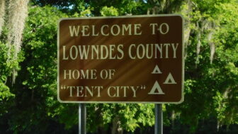 A sign reads "Welcome to Lowndes County. Home of Tent City," in White Hall, Alabama.
