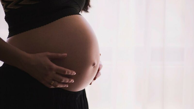 A pregnant woman holds onto her exposed stomach.
