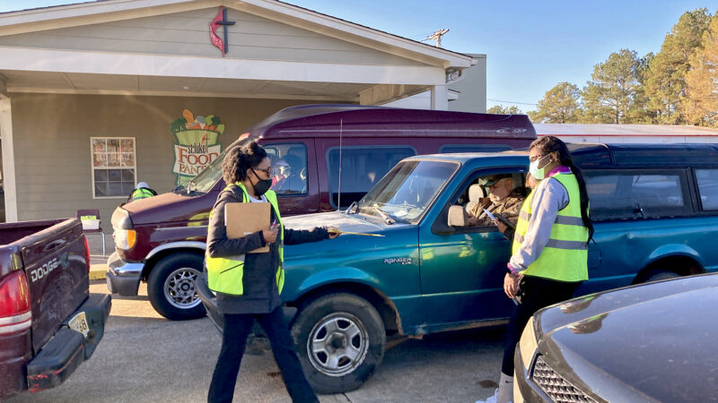 Two volunteers help a man in a green pickup truck receive food and supplies at Saint Luke's Food Pantry in Tupelo, Mississippi.