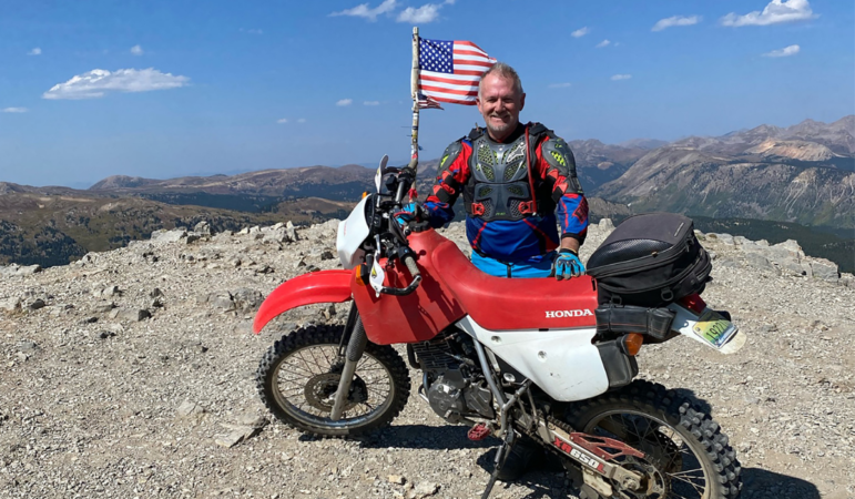 Jim Parsons stands atop American Flag Mountain after he climbed it on his dirt bike.