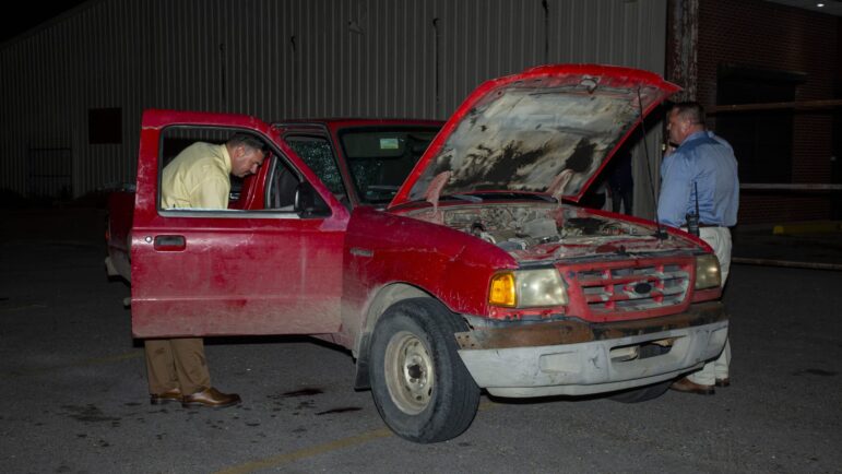New Orleans Police detectives look inside a damaged, red pickup truck at the scene of a homicide on April 22, 2022.