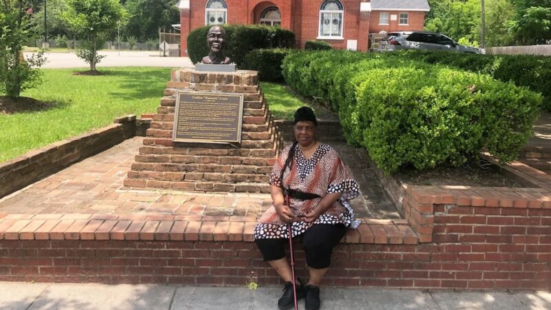 Descendant Vernetta Henson sits outside Union Baptist Church in Africatown. The church was started by Clotilda survivors in 1869. To her left is the bust of Cudjoe Lewis, one of Africatown's founders.