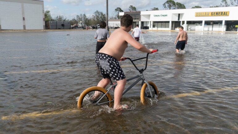 In this file photo, children ride bikes and march through floodwaters in the parking lot of a Dollar General in Terrebonne Parish, Louisiana after Hurricane Ida blew through the region, Aug. 30, 2021.