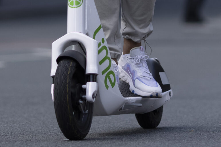 Close up of a person's feet and ankles riding a Lime e-scooter.