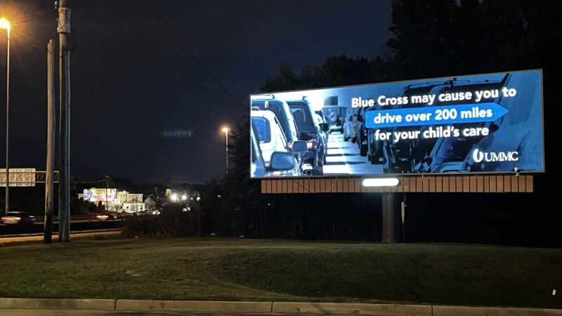 A billboard placed by UMMC in Jackson, Mississippi reads "Blue Cross may cause you to drive over 200 miles for your child's care."