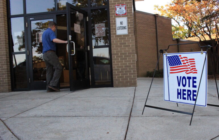 A man walks inside an entrance to a polling place next to a sign that reads "VOTE HERE."