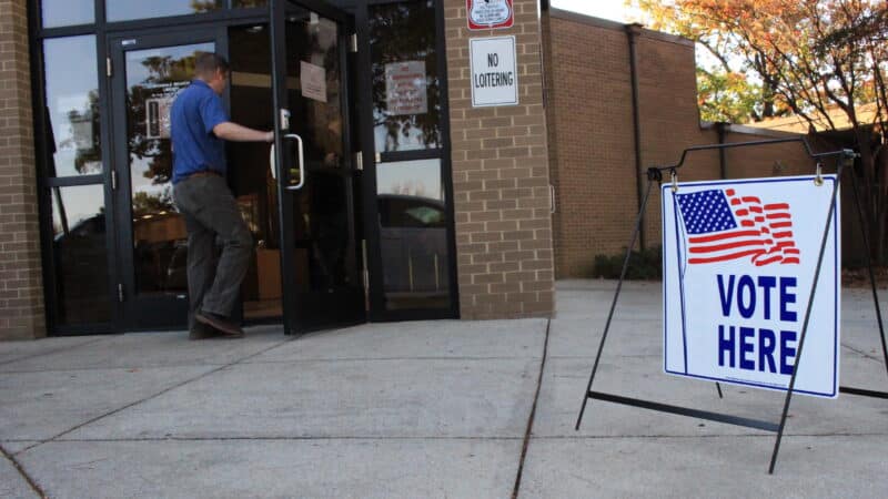 A man walks inside an entrance to a polling place next to a sign that reads "VOTE HERE."