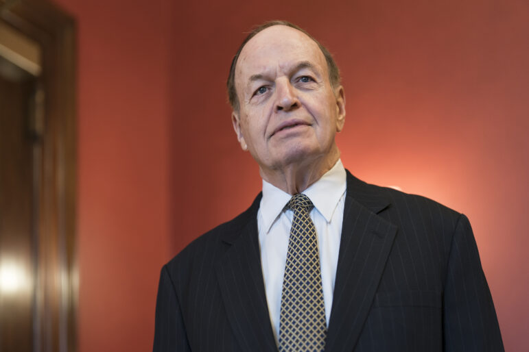 Alabama Senator Richard Shelby stands in front of an orange wall.
