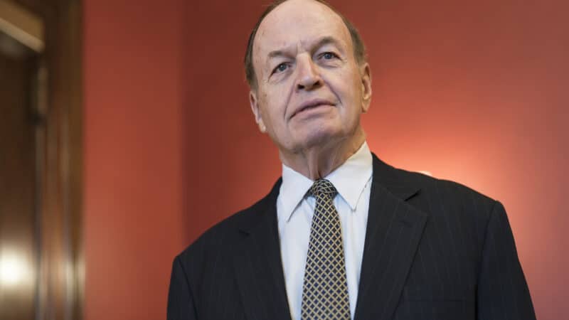 Alabama Senator Richard Shelby stands in front of an orange wall.