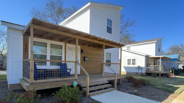 a white modular home with a wood porch stands near a sidewalk in Titusville.