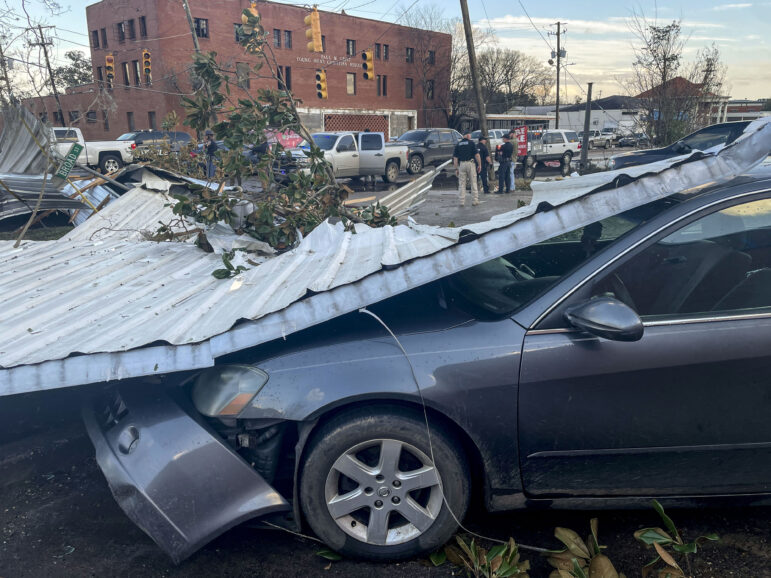 A large piece of metal on top of a car with more tornado debris in the background.