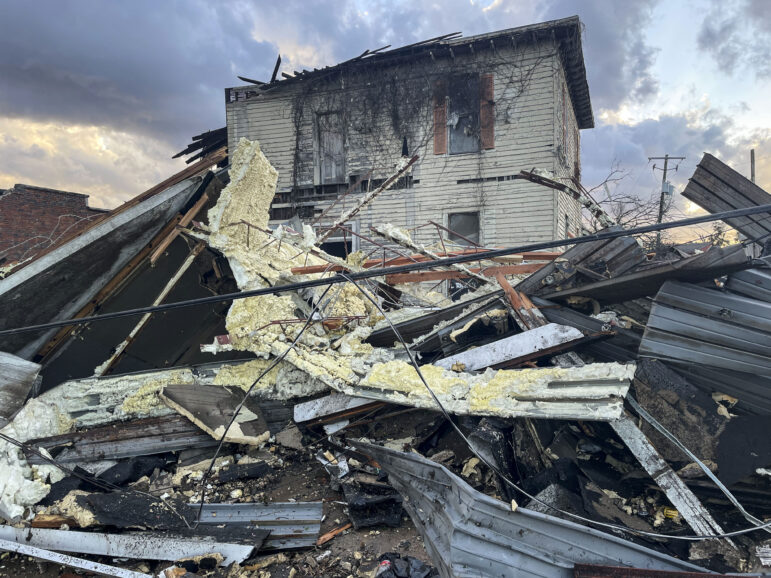 An old house is surrounded by tornado debris — pieces of metal and home insulation.