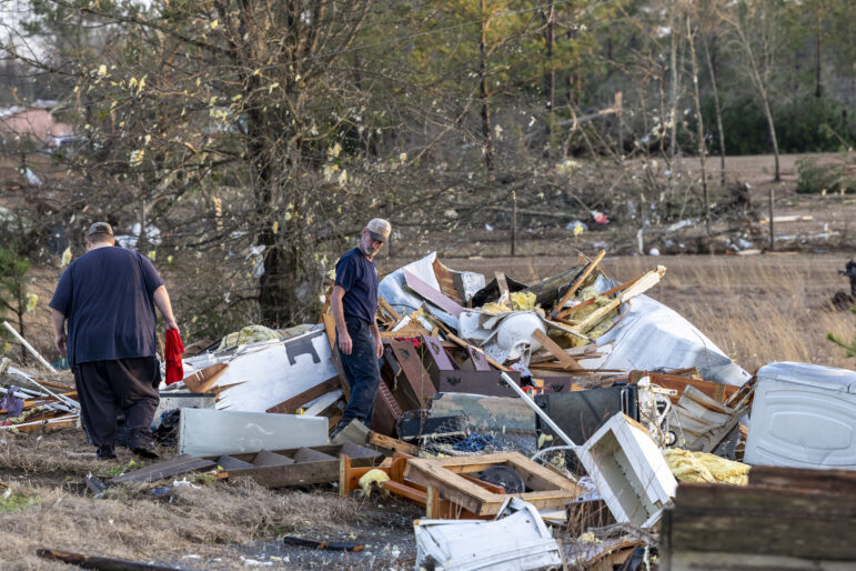Two men walk among debris piled up by a tornado.