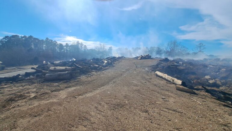 Smoke rises above the vast site covered with dirt and logs.