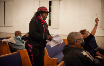 An African American woman stands up to speak at a meeting.
