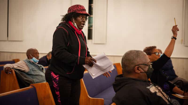 An African American woman stands up to speak at a meeting.