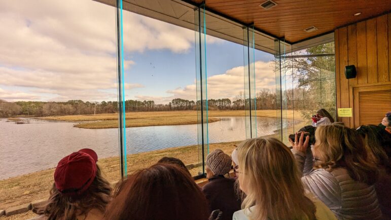 People gather by a glass paneled window in an observation room to see cranes.