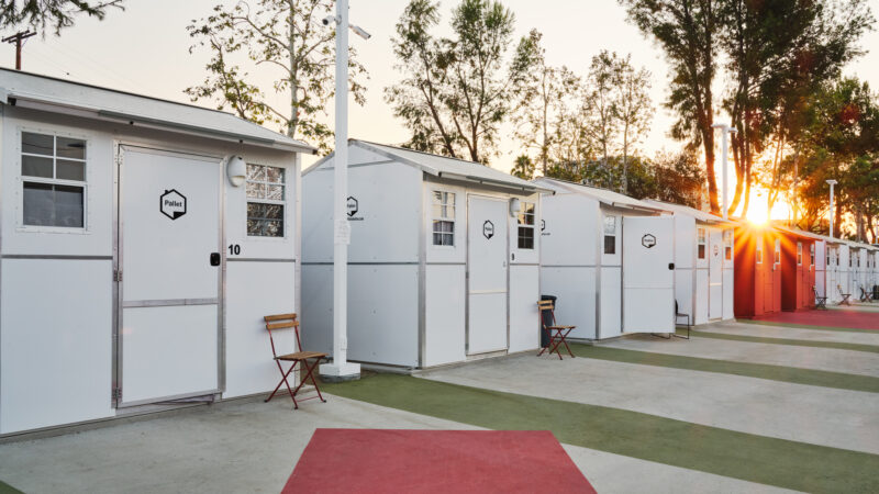 A row of prefabricated tiny homes are shown on a painted concrete lot.