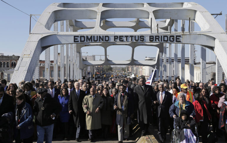 A large group of people, including Joe Biden and John Lewis, walk across the Edmund Pettus Bridge in Selma.
