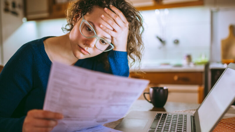 Young brunette curly female reading her tax papers, looking stressed.