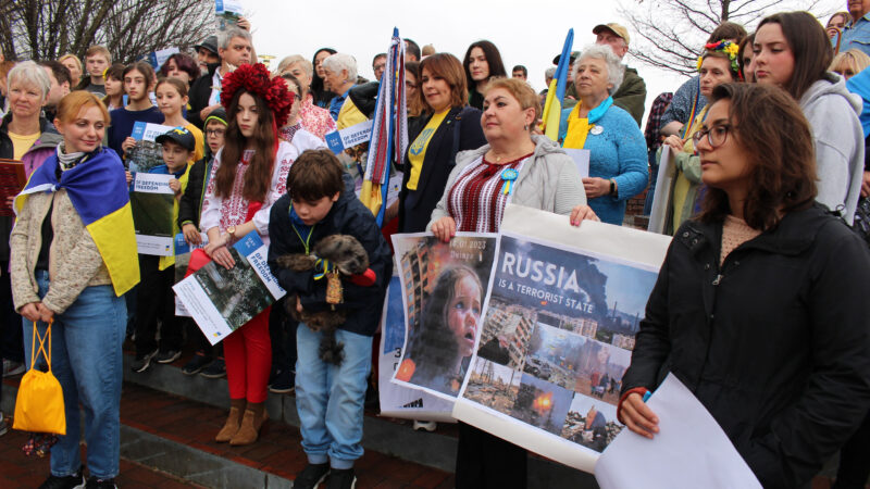 A group of people stand holding signs and Ukraine flags.
