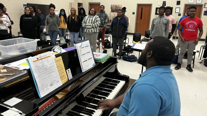 A man plays the piano while high school students sing in class