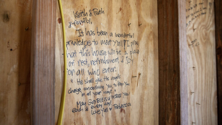 Ruth Crosby writes bible verses on the walls and studs of her home as it is being rebuilt. She was surprised to find similar messages from Amish volunteers who helped frame and put a roof on her new home.