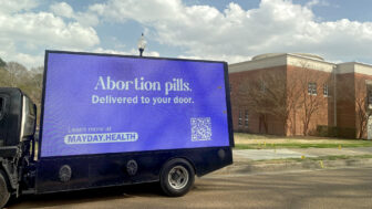 A mobile billboard sponsored by Mayday.Health shares the message "Abortion pills. Delivered to your door." over a blue background. It also shares a QR code and website information for Mayday.Health.