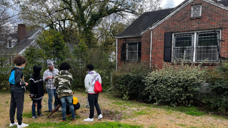 Students stand in front of slightly rundown house