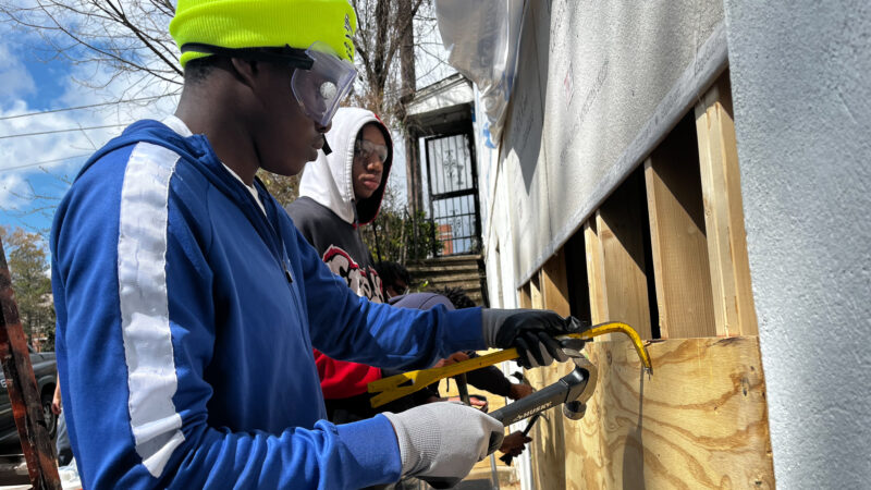 Student holds hammer and crowbar working on house