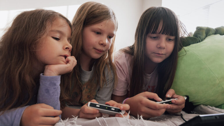 Viktoriia Vyshyvanyuk, Zoya Pritchett and Ioanna Vyshyvanyuk play a video game together.