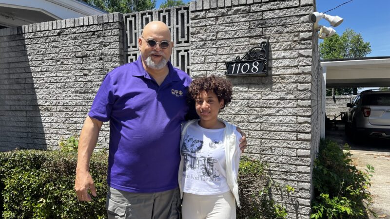 grandfather and granddaughter stand outside their home