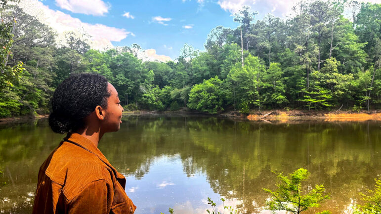 A woman looks across a pond surrounded by trees.