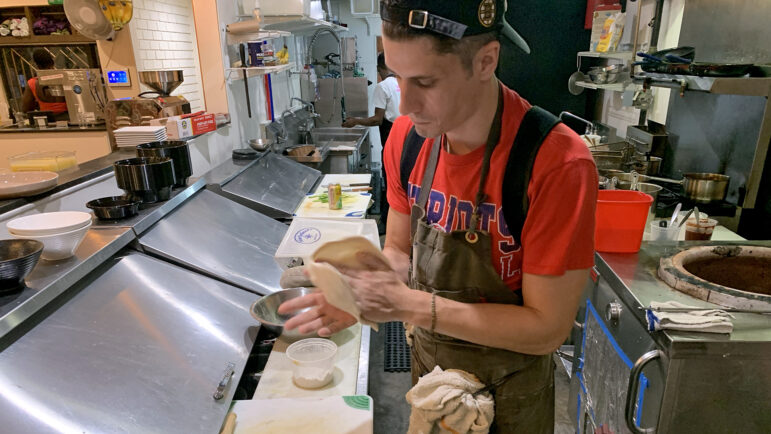 Tyler Stuart prepares to insert naan bread dough into the tandoori oven behind him in New Orleans on November 18, 2023.