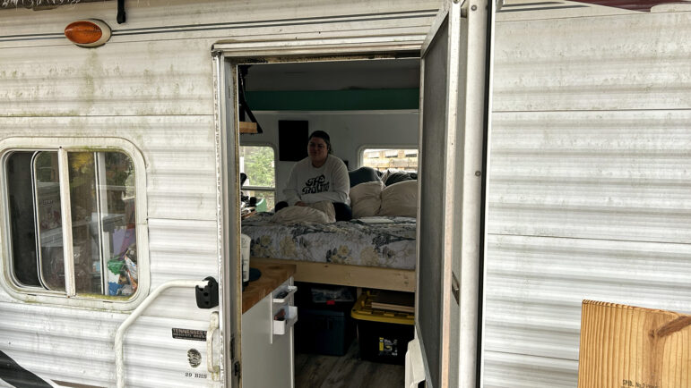 Gabbie Price can be seen sitting on her bed from the open front door of her camper home in Moody, Alabama, on March 15, 2024.