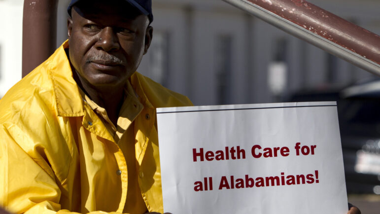 In this file photo, Jerry Burnet, of Huntsville, Ala., holds up a sign in support of the expansion of Medicaid in front of the State House as the first day of the Alabama Legislature begins on Tuesday, Jan. 14, 2014, in Montgomery, Ala.