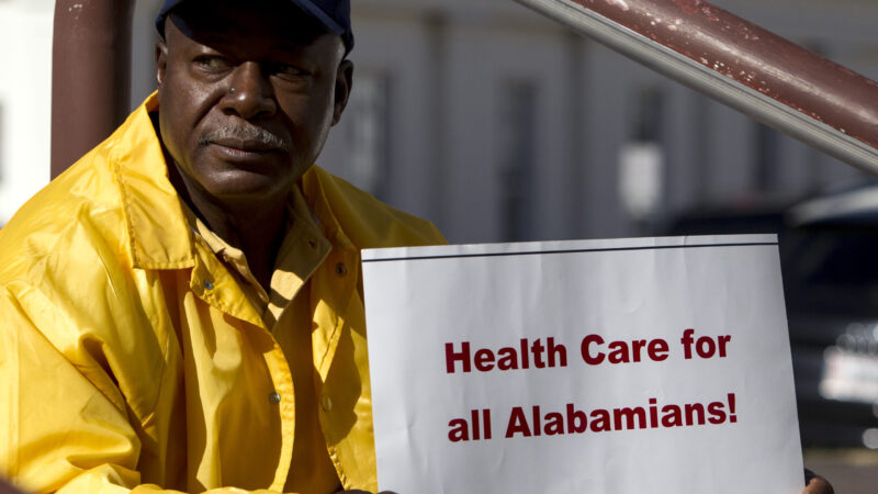 In this file photo, Jerry Burnet, of Huntsville, Ala., holds up a sign in support of the expansion of Medicaid in front of the State House as the first day of the Alabama Legislature begins on Tuesday, Jan. 14, 2014, in Montgomery, Ala.