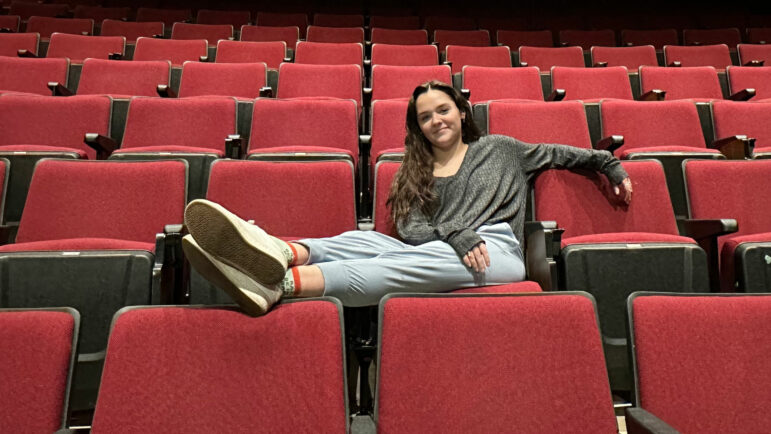 Lily Kate relaxes in an audience chair at the Troy Trojan Center Theater with her feet up on another seat.