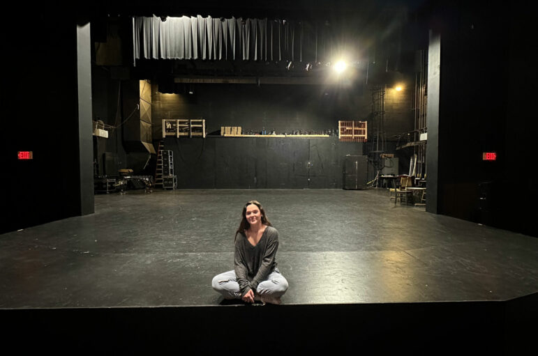 Lily Kate sits cross-legged at the edge of the stage at the Troy Trojan Center Theater.