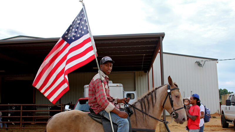 JayBo mounts his horse, Spook, while holding an American flag at the inaugural Pontotoc Juneteenth Horse Show in Pontotoc, Mississippi, on June 19, 2024.