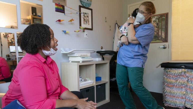 Capri Isidoro, of Ellicott City, Md., left, watches as Ann Faust, an International Board Certified Lactation Consultant (IBCLC), holds her one-month-old daughter Charlotte, Monday, May 23, 2022, as part of a lactation consultation in Columbia, Md., at Baby and Me Lactation Services.