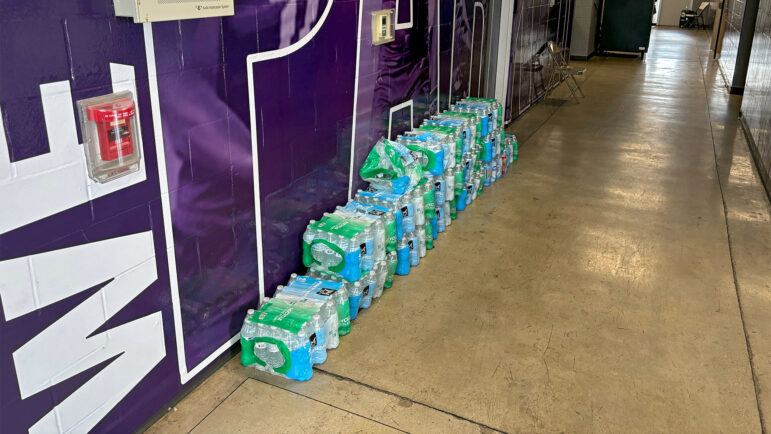 Cases of water to be used by student-athletes and coaching staff during football practice are stacked against a wall inside the A.H. Parker High School field house on Aug. 22, 2024.