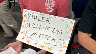 An LGBTQ+ advocate holds a sign that reads “Queer well-being matters” during a Moms For Liberty town hall meeting on Title IX at the North Shelby County Library in Pelham, Alabama, on July 1, 2024.