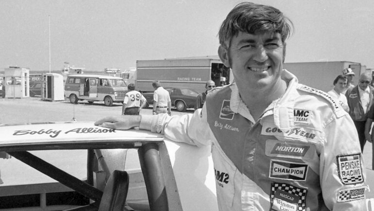 Bobby Allison stands beside his car and talks with the press after winning the pole position during qualifying for the 500 mile grand national stock car race at Pocono Raceway.