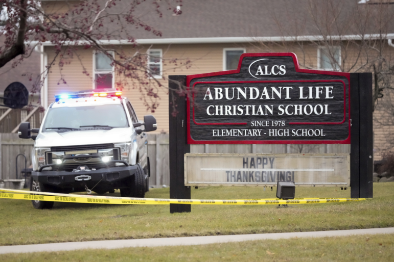 This photo shows a large wooden sign that says "Abundant Life Christian School" on it. An emergency vehicle is parked on the grass next to the sign. Yellow caution tape extends across the photo.