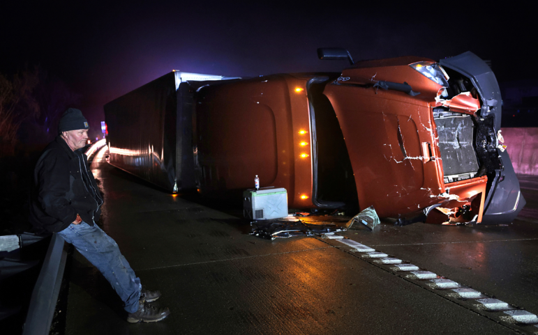 Mark Nelson, of Wis., waits with his tractor-trailer after it overturned during high winds and a possible tornado on Interstate 44 westbound at Villa Ridge, Mo., on Friday.