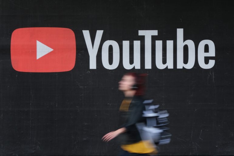A young woman wearing headphones walks past a billboard advertisement for YouTube in 2019 in Berlin, Germany.